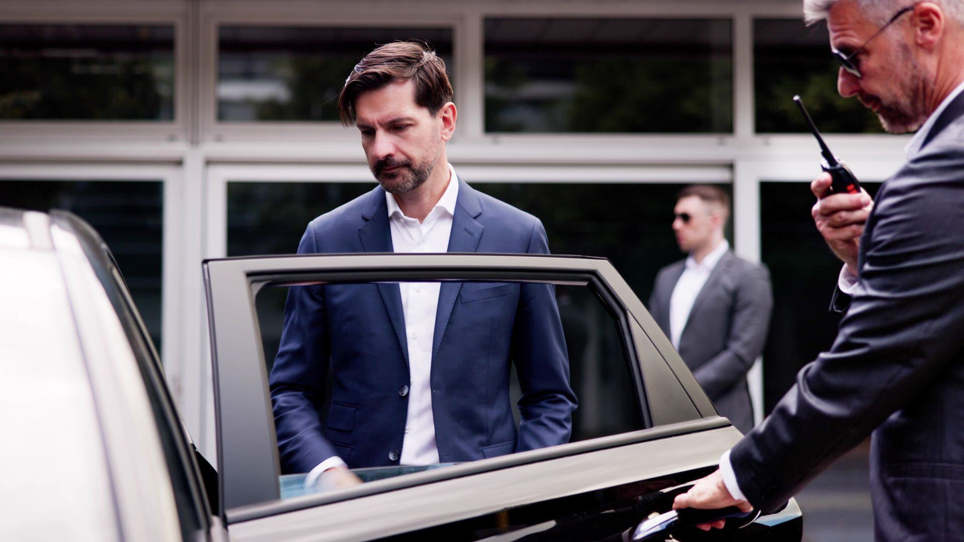 A protection detail stands watch as an executive gets in a vehicle